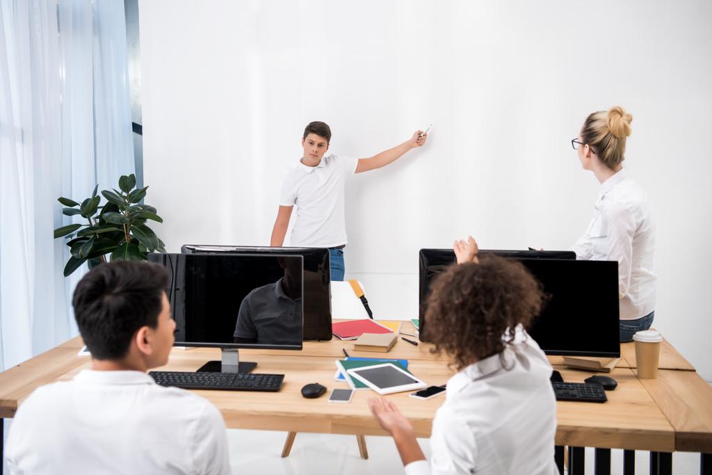 joven adolescente apuntando en la pizarra blanca en el aula con los estudiantes
 - Foto, Imagen