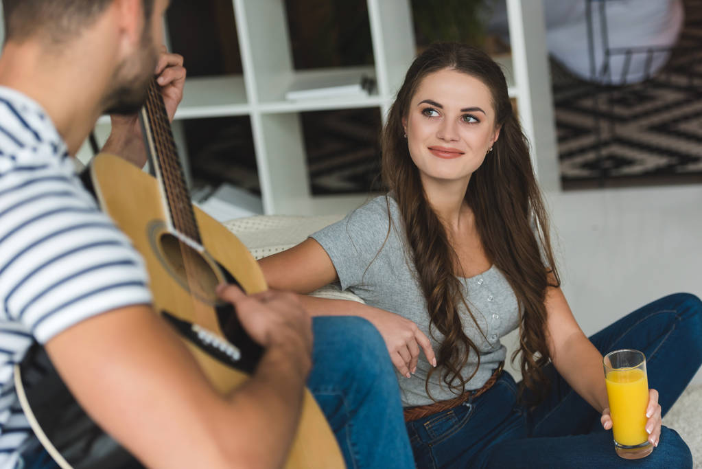 man gitaarspelen voor vriendin terwijl ze zittend op de vloer met SAP - Foto, afbeelding