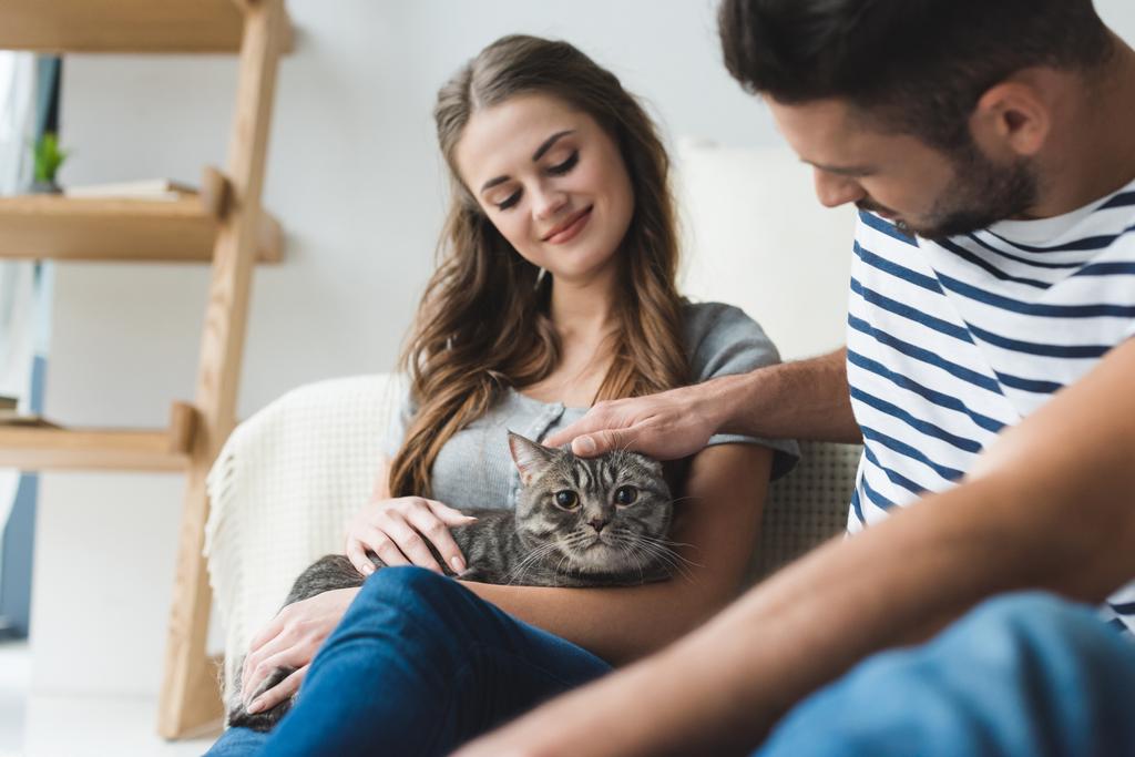 happy young couple petting cat at home while sitting on floor - Photo, Image