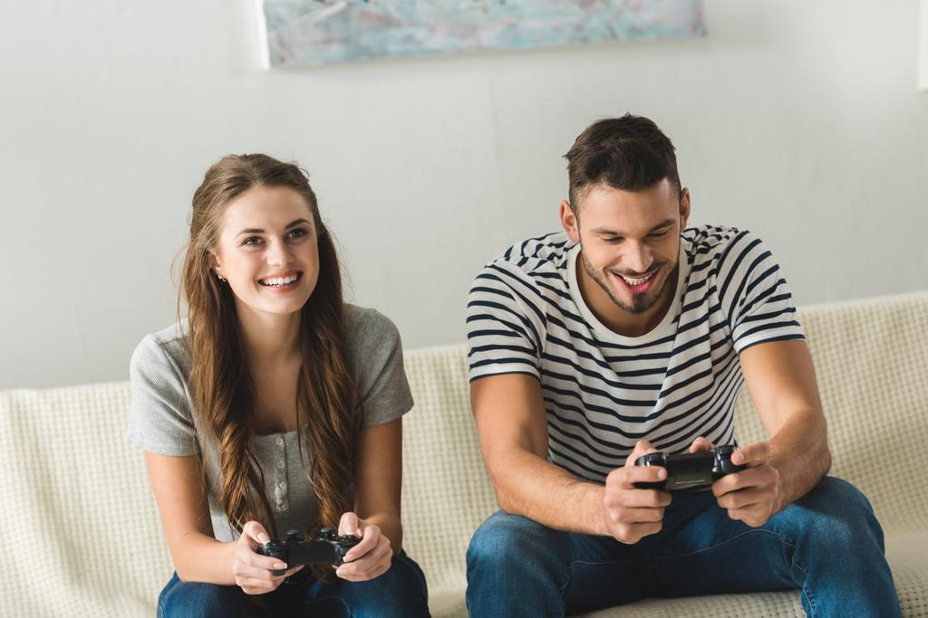 smiling young couple playing games with gamepads at home - Photo, Image