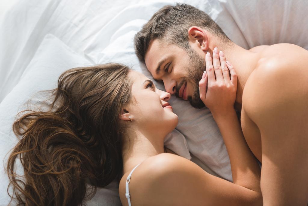vista superior de casal jovem sorridente abraçando na cama de manhã
 - Foto, Imagem