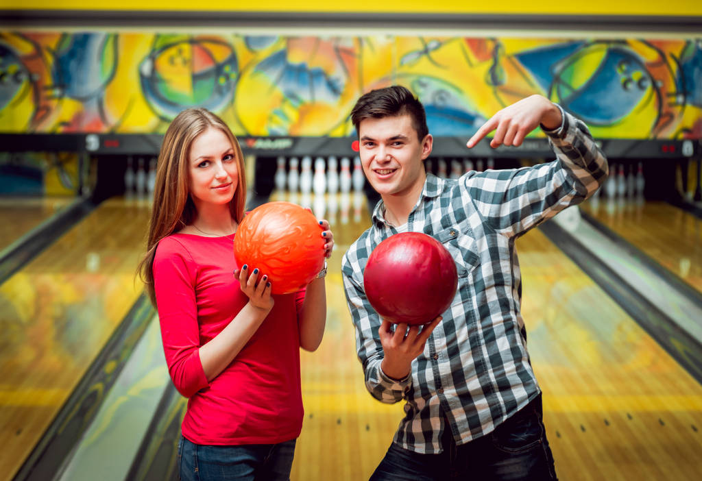 Krásná dívka a mladý muž na bowlingu s míčky - Fotografie, Obrázek