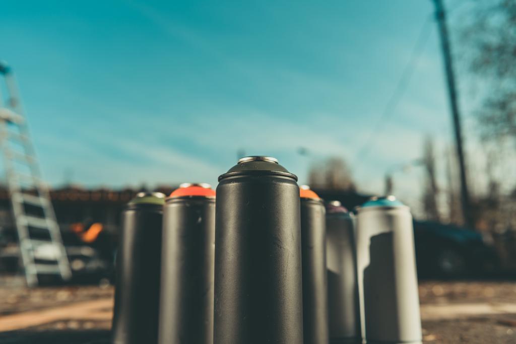 cans with colorful spray paint for graffiti on asphalt with blue sky on background - Photo, Image