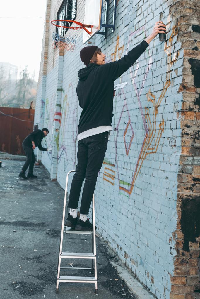 hombre de pie en la escalera y pintando graffiti colorido en la construcción
 - Foto, imagen