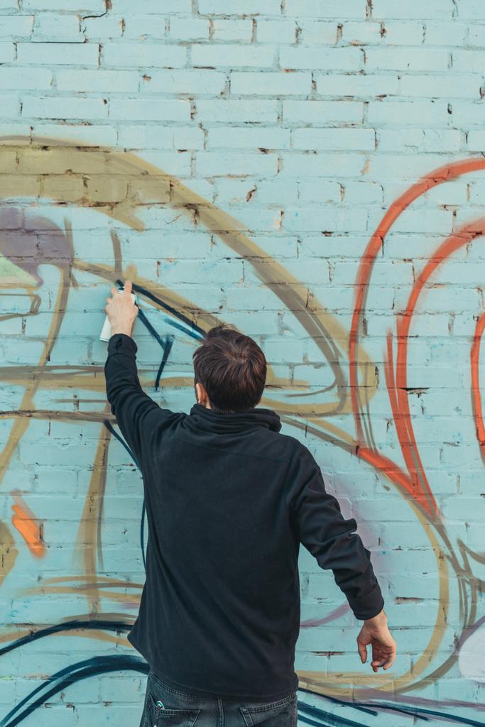 back view of man painting colorful graffiti on wall - Photo, Image