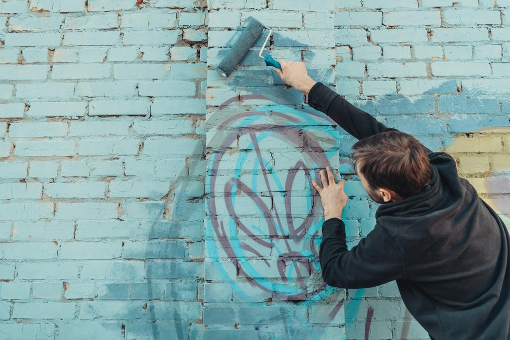 αρσενικός καλλιτέχνης δρόμου ζωγραφική πολύχρωμα γκράφιτι στον τοίχο με ρολό - Φωτογραφία, εικόνα