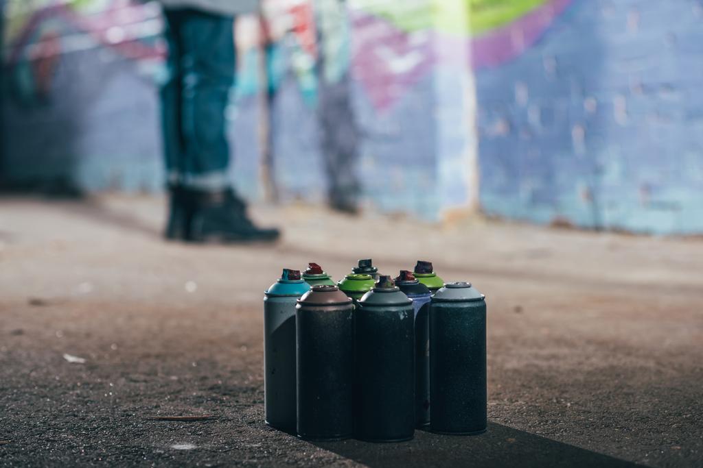baixa seção de artista de rua pintando graffiti à noite, latas com tinta aerossol em primeiro plano
 - Foto, Imagem
