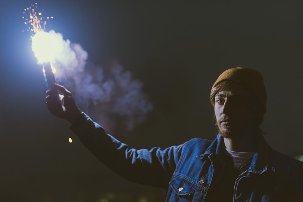 Mann hält in der Nacht Rauchbombe mit Funken in der Hand - Foto, Bild