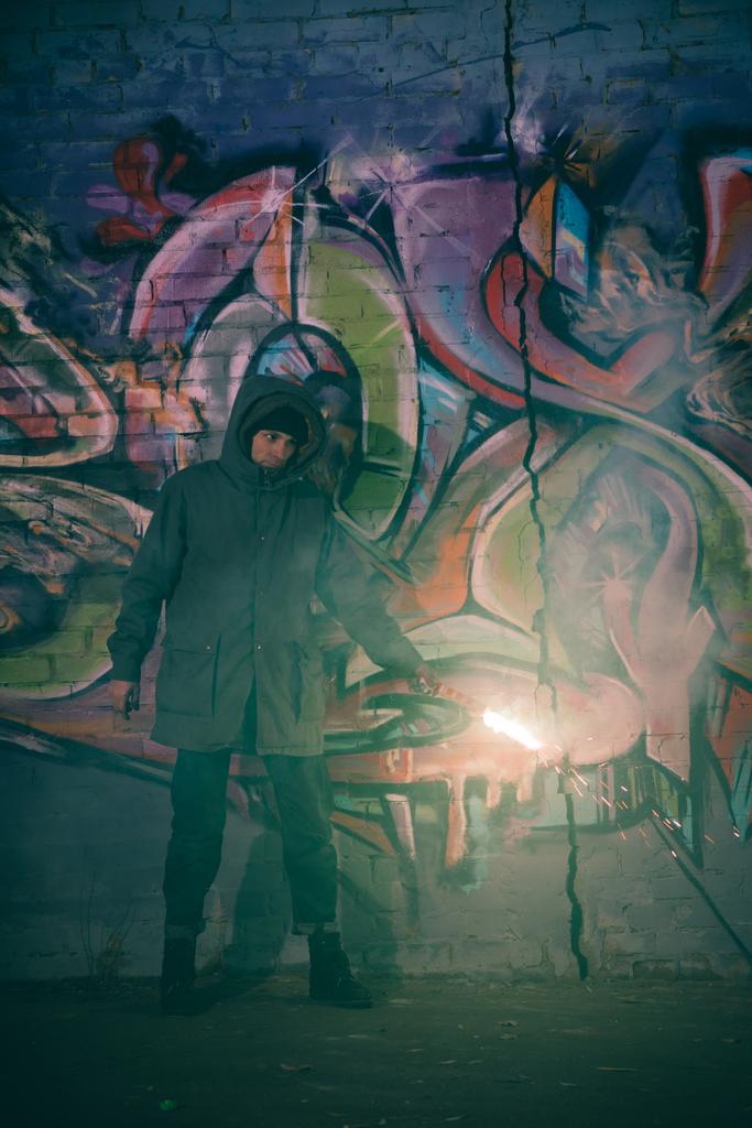 man holding smoke bomb and standing against wall with graffiti at night - Photo, Image