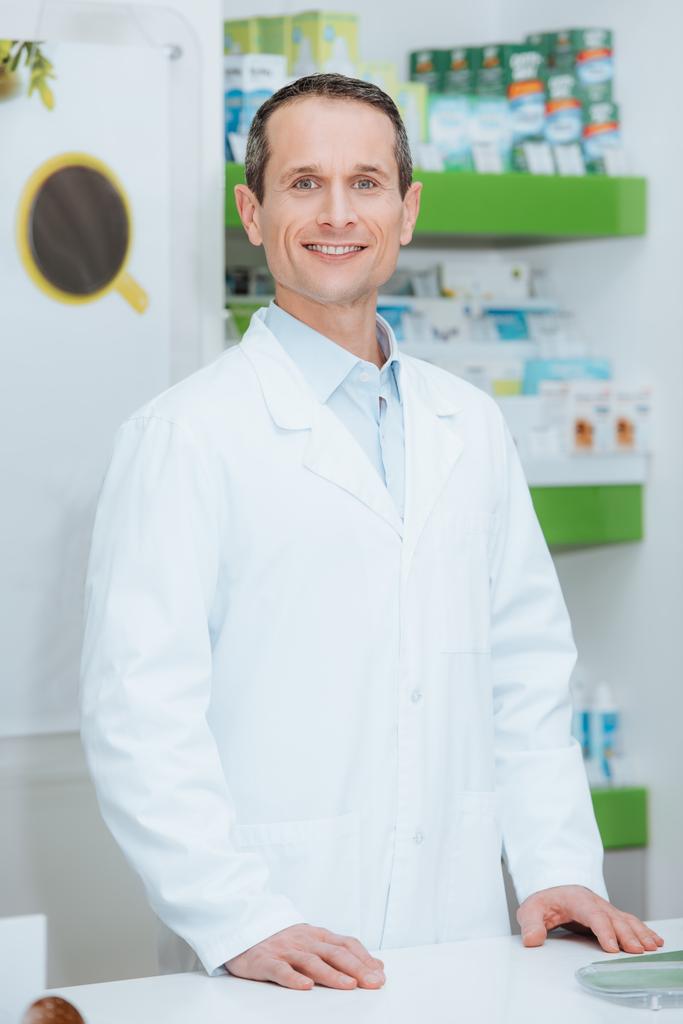 retrato de optometrista sorridente em casaco branco em pé no balcão em óptica
 - Foto, Imagem