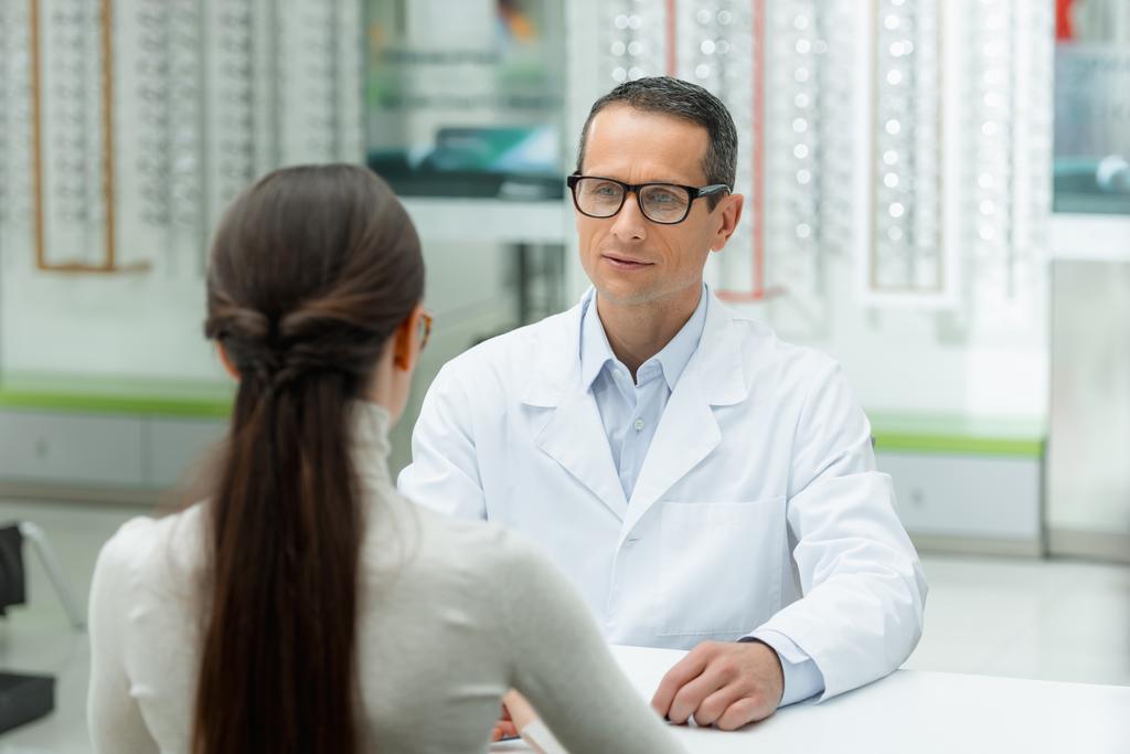 enfoque selectivo de la vista lateral del oftalmólogo y la mujer joven teniendo conversación en óptica
 - Foto, imagen