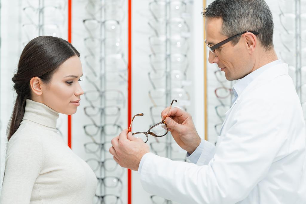 puolella näkymä silmälääkäri auttaa naista valitsemaan silmälasit optiikassa
 - Valokuva, kuva