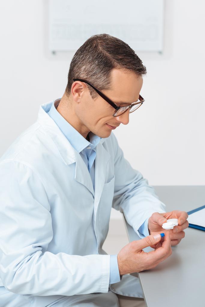 sivukuva silmälääkäri tarkastellaan piilolinssi käsissä istuessaan työpaikalla klinikalla
 - Valokuva, kuva