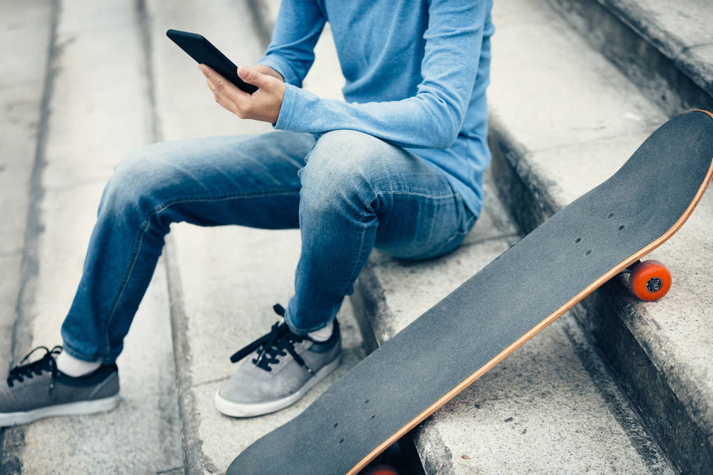 met behulp van smartphone zittend op stad trap met skateboard skateboarder - Foto, afbeelding
