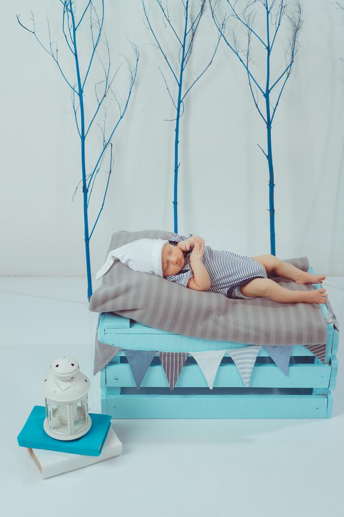 entzückendes Neugeborenes in Body und Hut schlafend auf Holzkiste mit Laterne in der Nähe - Foto, Bild