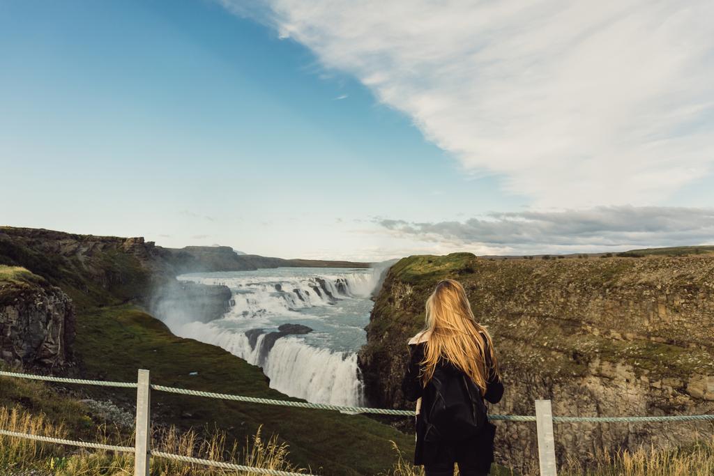vista posterior de la joven mujer mirando la cascada majestuosa escénica en Islandia
  - Foto, imagen