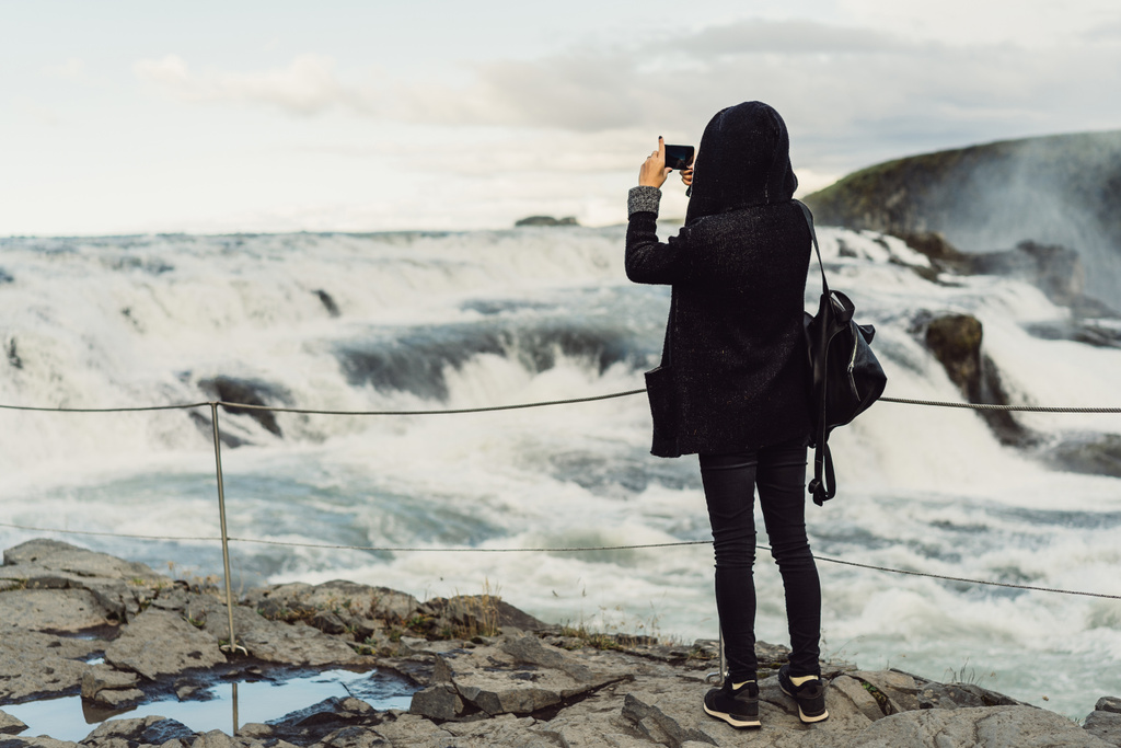 πίσω όψη του νεαρή γυναίκα, φωτογραφίζοντας μεγαλοπρεπής Καταρράκτης στην Ισλανδία  - Φωτογραφία, εικόνα