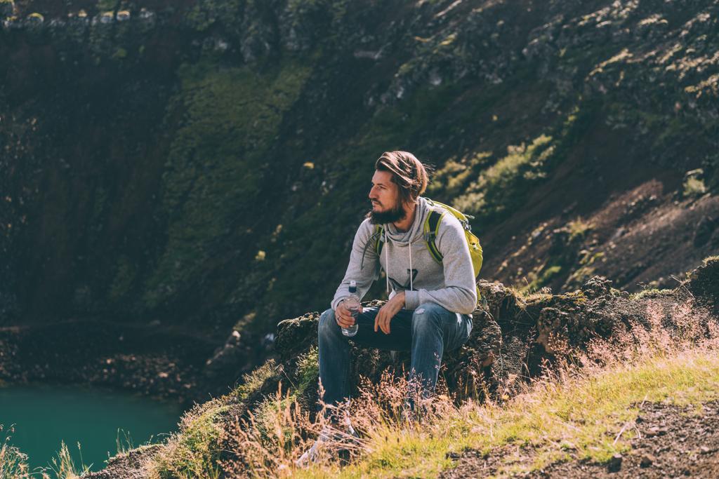 joven barbudo sentado en la roca y mirando el hermoso lago del cráter en Islandia
  - Foto, Imagen