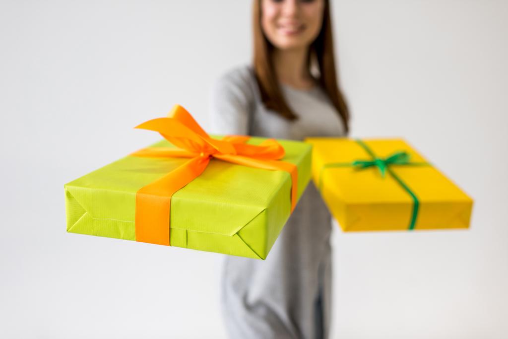 вибірковий фокус усміхненої молодої жінки, що показує подарунки в руках
 - Фото, зображення