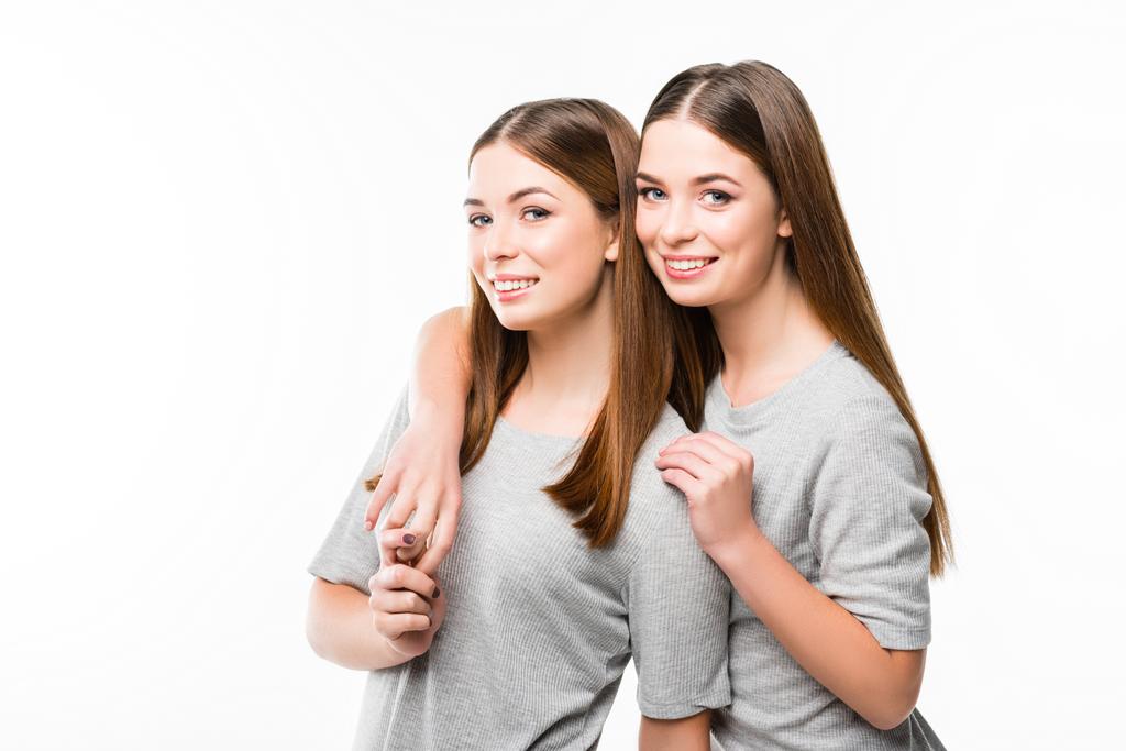 muotokuva nuorista hymyilevistä kaksosista nojaamassa toisiinsa ja katselemassa kameraa, joka on eristetty valkoisella
 - Valokuva, kuva