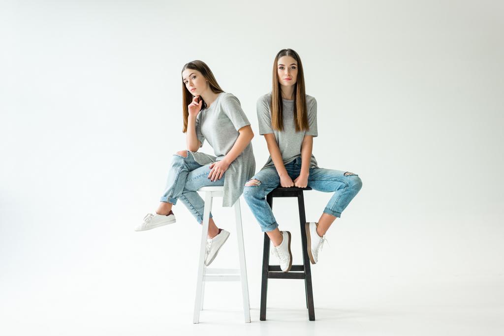 fiatal ikrek látszó-on fényképezőgép-ülve székek hasonló ruházat - Fotó, kép