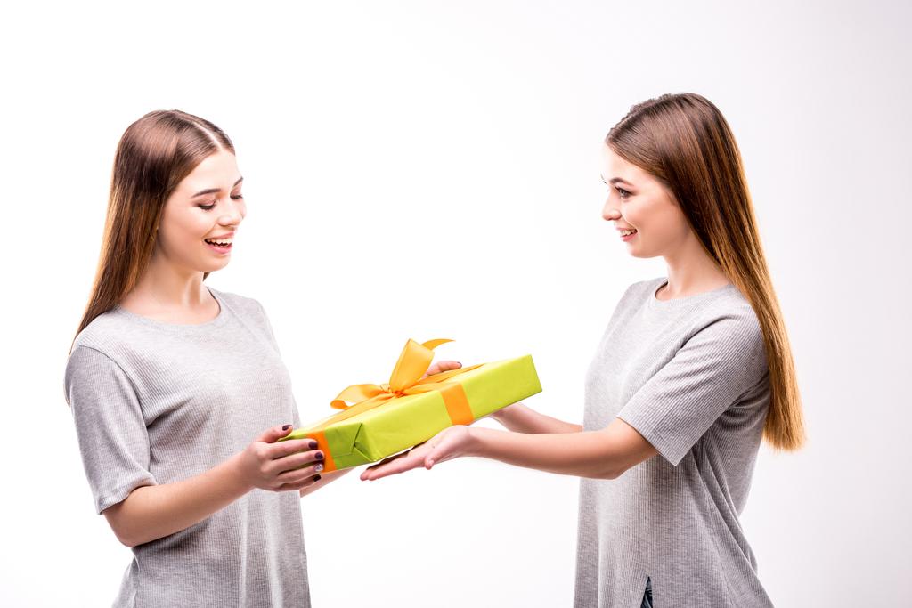 Widok z boku uśmiechający się kobiety, prezentując owinięty prezent dla siostry bliźniaczki - Zdjęcie, obraz
