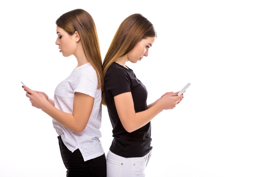 side view of twins standing back to back and using smartphones isolated on white - Photo, Image