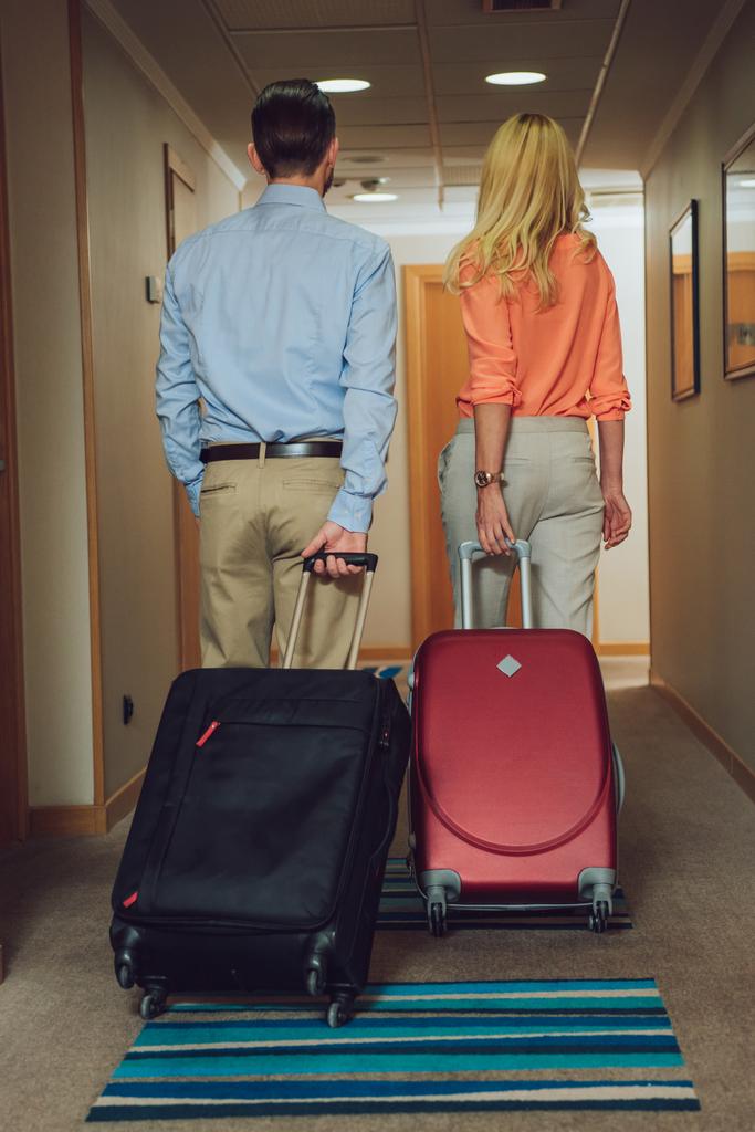 vista trasera de pareja de mediana edad con maletas caminando en el pasillo del hotel
 - Foto, imagen