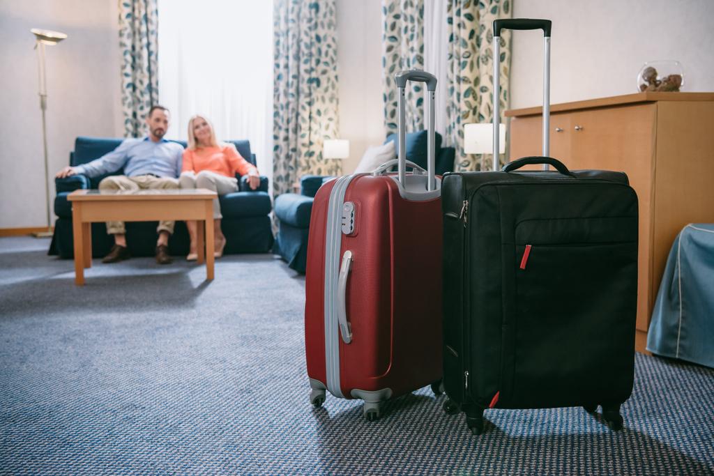 Nahaufnahme von zwei Koffern und reifem Paar auf Sofa im Hotelzimmer - Foto, Bild