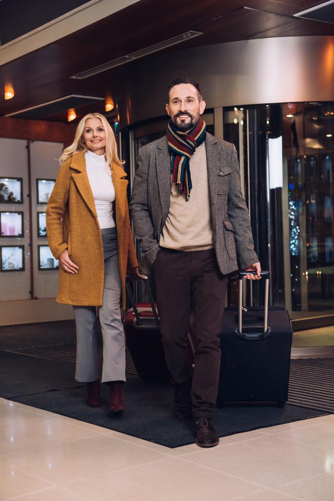 улыбающаяся зрелая пара с чемоданами, покидающими отель
 - Фото, изображение