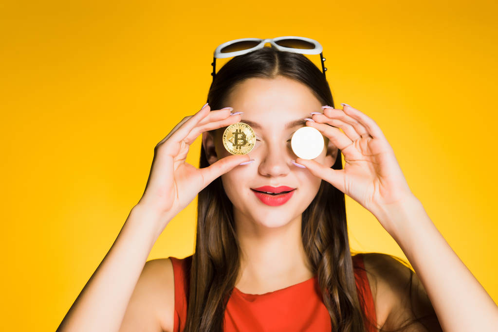 usměvavá mladá dívka s červenou rtěnku drží zlaté bitcoiny ve svých rukou, zavře oči - Fotografie, Obrázek