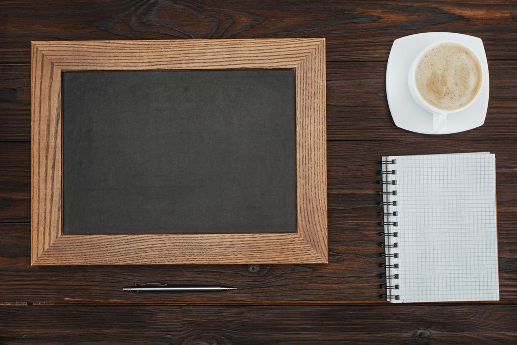 tendido plano con pizarra vacía, taza de café, cuaderno en blanco y pluma en la mesa de madera oscura
 - Foto, imagen