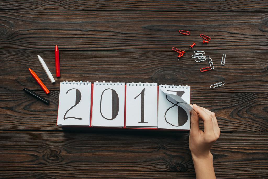 ritagliato colpo di donna strappando parte del calendario 2018 anno con superficie di legno scuro come sfondo
 - Foto, immagini