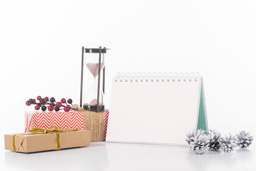 Nahaufnahme von leerem Kalender, Sanduhr, Tannenzapfen und verpackten Geschenken isoliert auf weiß - Foto, Bild