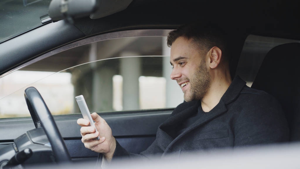 Houkutteleva liikemies istuu auton sisällä nauraen älypuhelimella matkan jälkeen
 - Valokuva, kuva