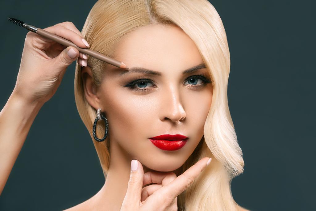 krásná blondýnka použití make-up obočí, izolované Grey - Fotografie, Obrázek