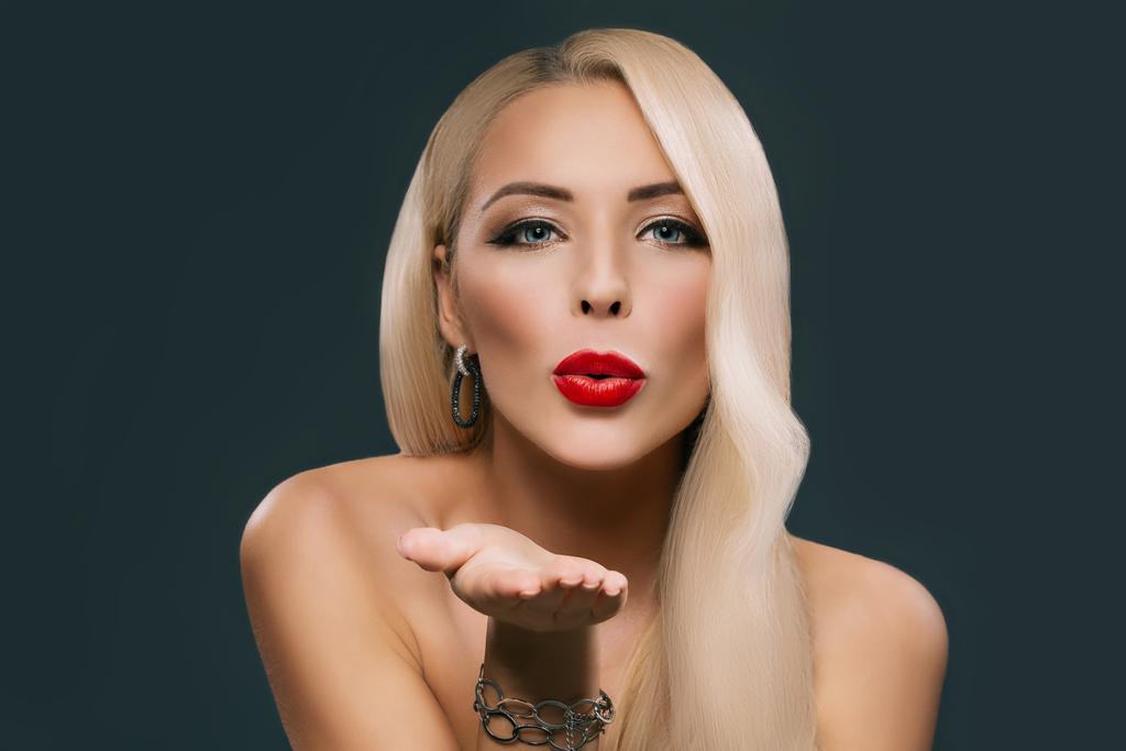 beautiful blonde woman with makeup and hairstyle blowing kiss, isolated on grey - Photo, Image