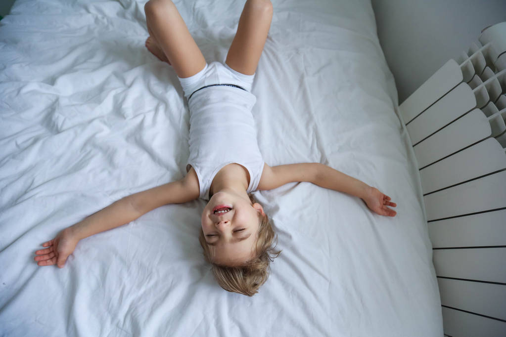 vista desde arriba en niño divirtiéndose acostado en la cama blanca
  - Foto, imagen