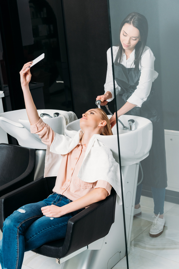 bella donna prendendo selfie mentre parrucchiere lavarsi i capelli al salone
 - Foto, immagini