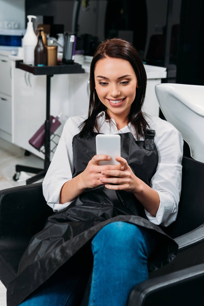 парикмахер сидит в кресле на работе и смотрит на смартфон
 - Фото, изображение