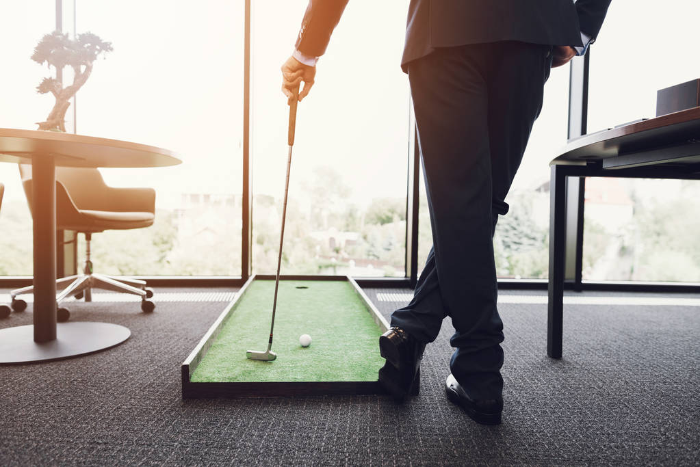 Близько. Чоловік у діловому костюмі грає в гольф в офісі
 - Фото, зображення