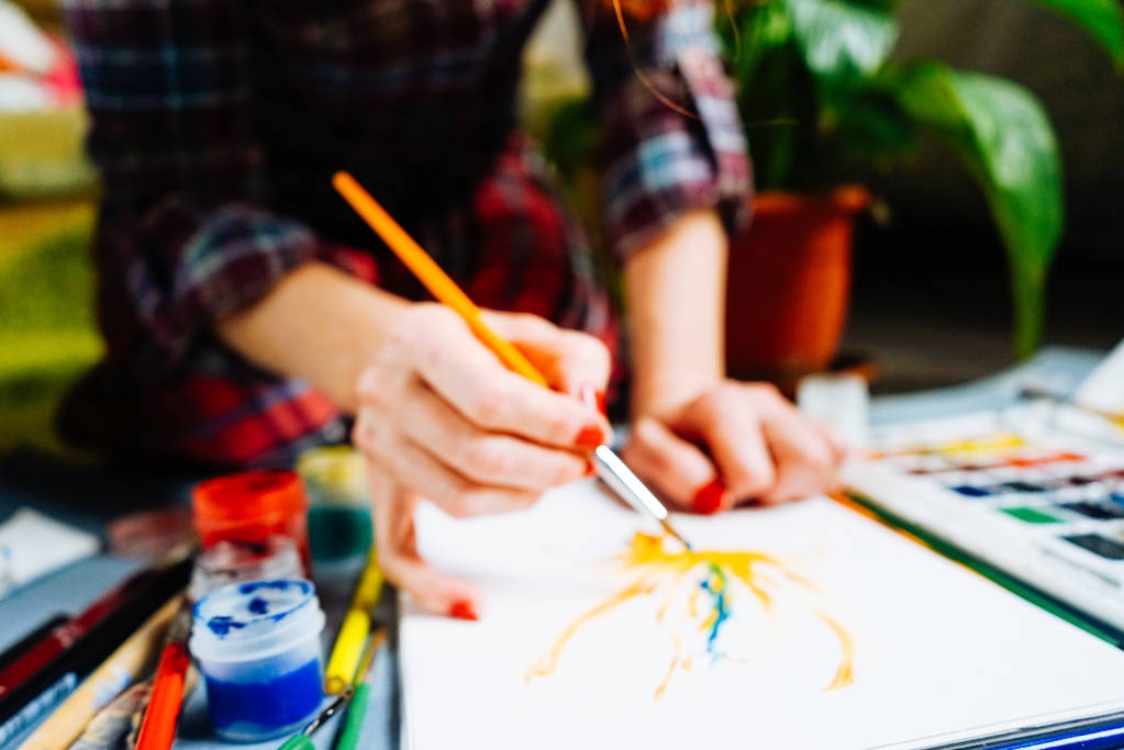 κορίτσι ζωγράφος ζωγραφίζει μια βούρτσα σε λευκό χαρτί, περιτριγυρισμένο από χρώματα watercolor και γκουάς - Φωτογραφία, εικόνα