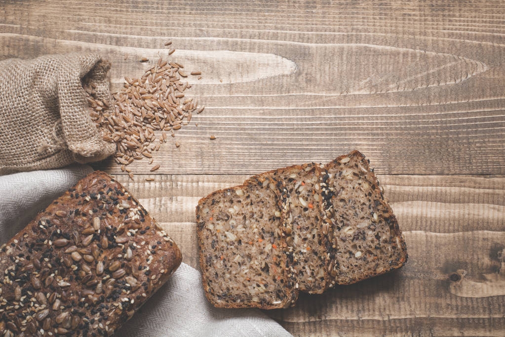 Ένα καρβέλι φρέσκο ρουστίκ ολικής αλέσεως ψωμί σίκαλης, κομμένο σε φέτες σε ένα ξύλινο ταμπλό, αγροτικών τροφίμων φόντο. - Φωτογραφία, εικόνα