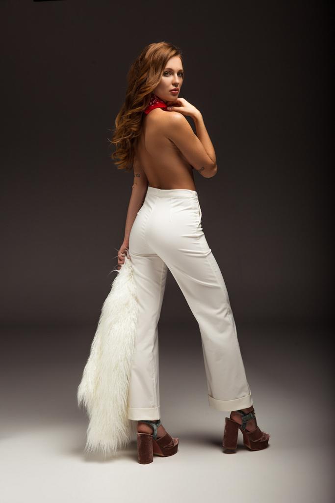 sexy Frau mit nacktem Rücken in weißen Hosen, die über die Schulter schaut - Foto, Bild