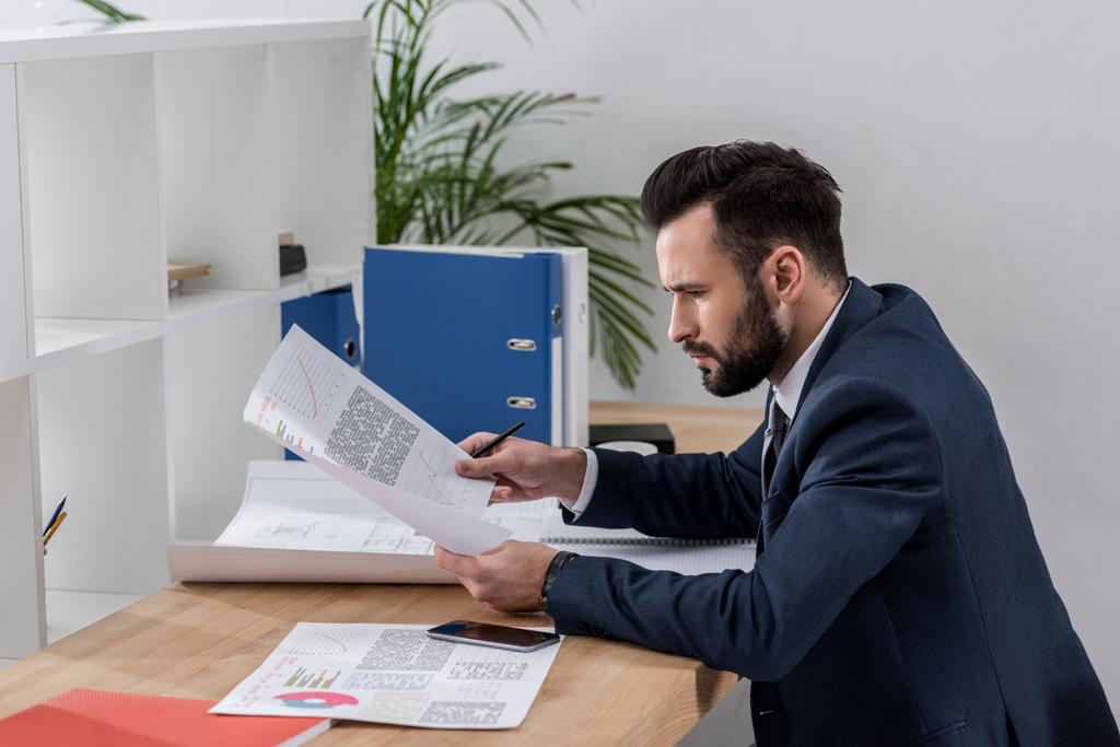 бизнесмен, сидящий за рабочим столом и просматривающий документы
 - Фото, изображение