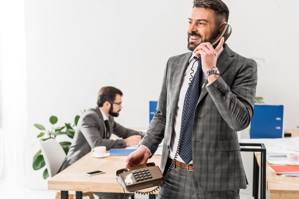 улыбающийся бизнесмен разговаривает по стационарному телефону в офисе
 - Фото, изображение