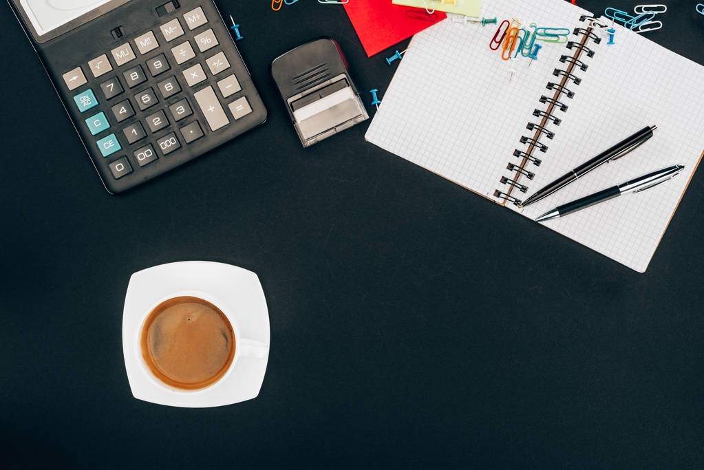 top view of cup of coffee, calculator and office supplies on black - Photo, Image