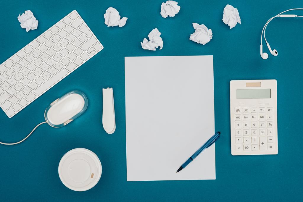 bovenaanzicht van een leeg vel papier met pen, rekenmachine, computermuis en toetsenbord op blauw - Foto, afbeelding