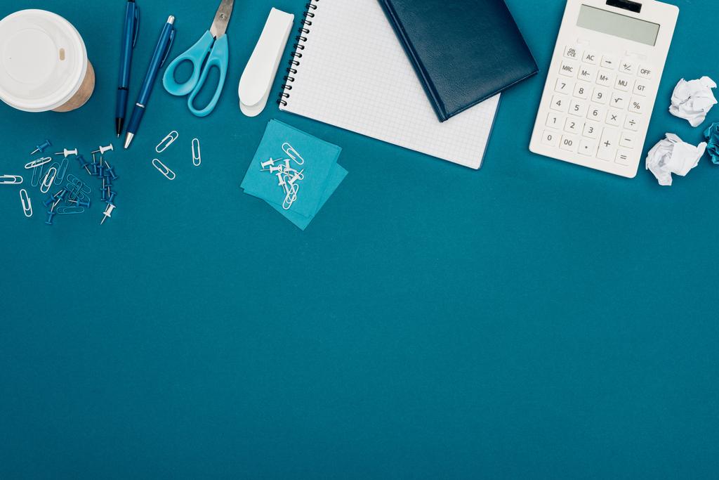 bovenaanzicht van rekenmachine, koffie te gaan en kantoorbenodigdheden op blauw - Foto, afbeelding