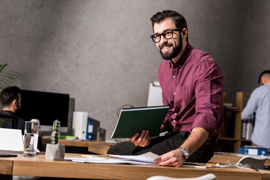 улыбающийся бизнесмен с документами и сидящий на столе
 - Фото, изображение